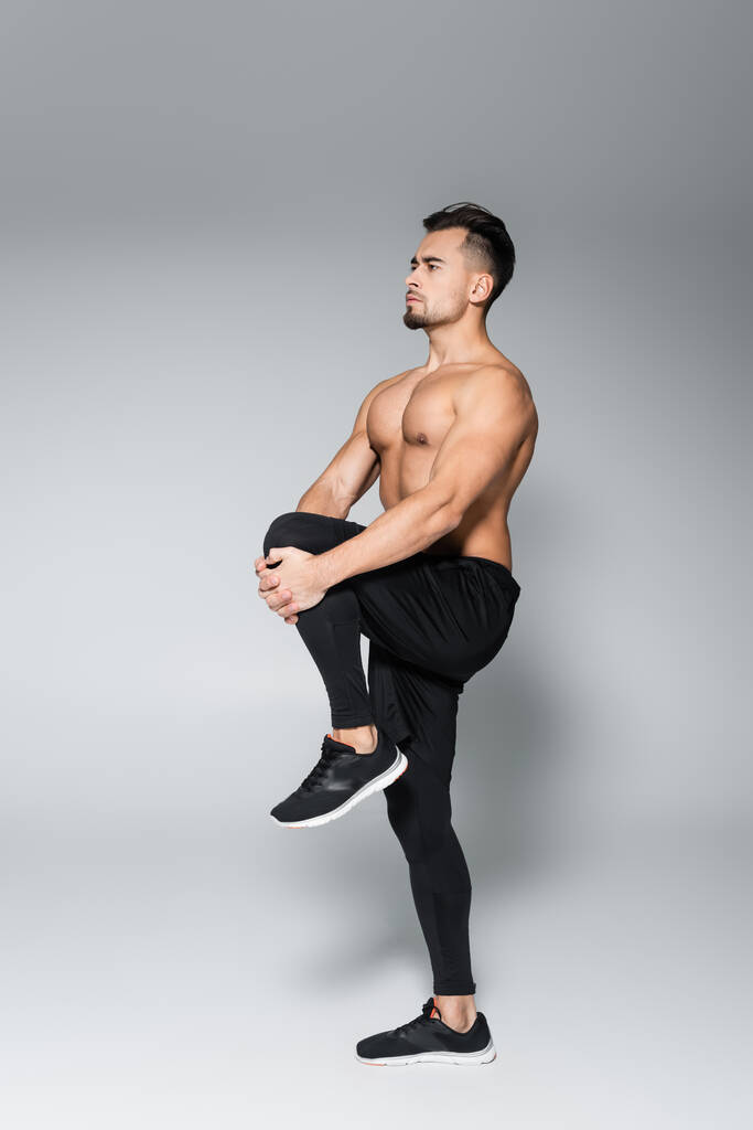 Volle Länge des jungen muskulösen Sportlers Stretching Bein auf grau - Foto, Bild