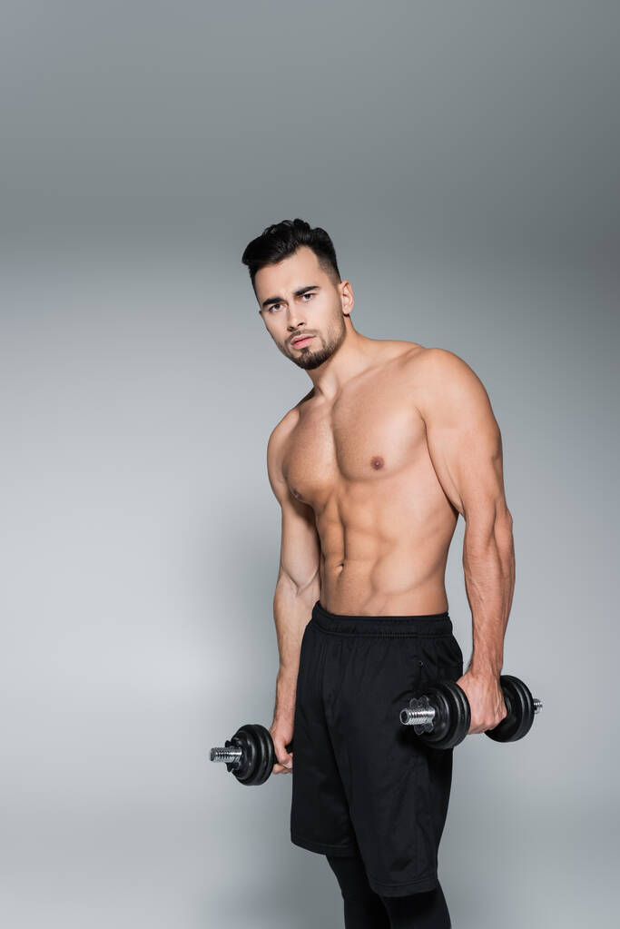 мускулистый и сильный спортсмен держит гантели на сером - Фото, изображение