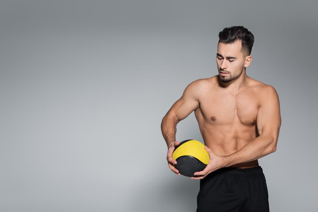 deportista musculoso y barbudo mirando la pelota en gris - Foto, Imagen