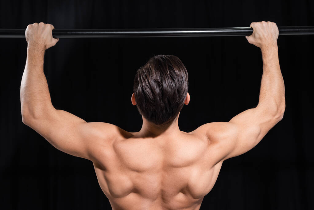 visão traseira do desportista muscular exercitando-se na barra horizontal isolada em preto  - Foto, Imagem