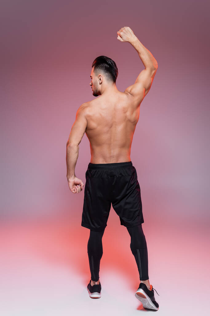 πίσω όψη του γυμνού άνδρα που δείχνει τους μυς και ποζάρει σε ροζ και γκρι   - Φωτογραφία, εικόνα