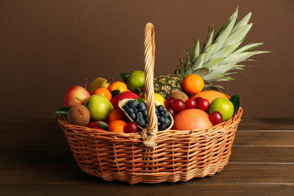 Συλλογή φρέσκων εξωτικών φρούτων σε ψάθινο καλάθι σε ξύλινο τραπέζι - Φωτογραφία, εικόνα