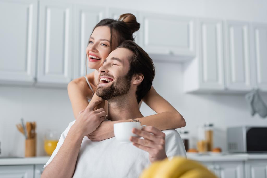 młody tatuaż kobieta przytulanie uśmiechnięty mężczyzna w kuchnia  - Zdjęcie, obraz