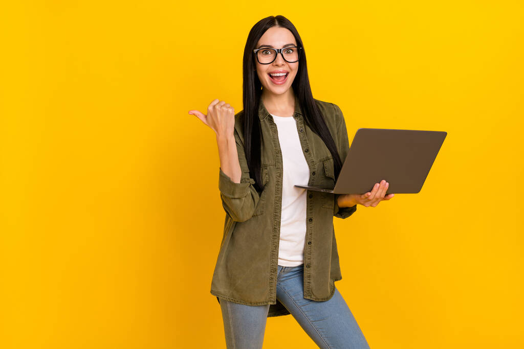 Zdjęcie hr młoda dama trzymać laptop wskazują promo nosić okulary khaki koszula izolowane na żółtym tle - Zdjęcie, obraz