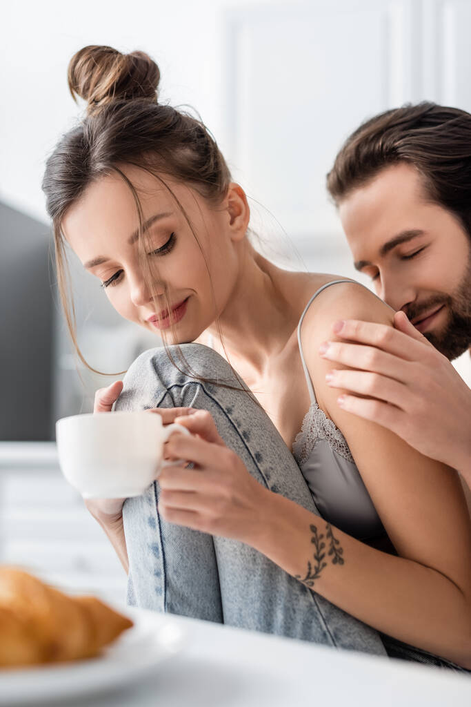 lachende man met baard aanraken hand van getatoeëerde vriendin met kopje koffie - Foto, afbeelding