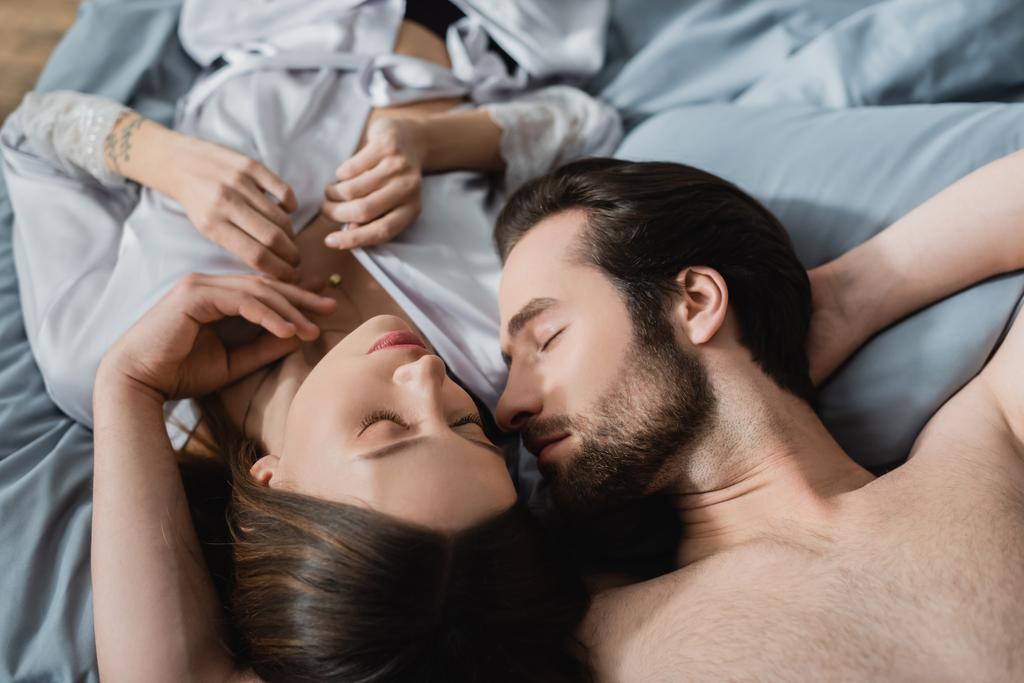 высокий угол зрения на татуированную женщину, лежащую с мужчиной без рубашки на кровати - Фото, изображение