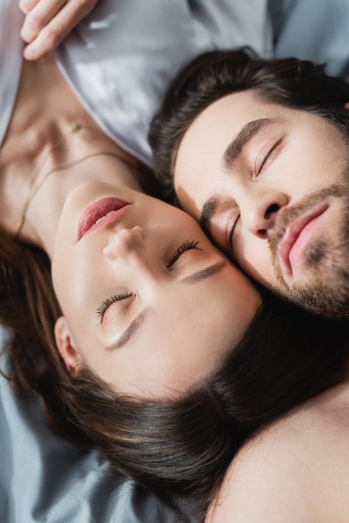 πάνω όψη της νεαρής γυναίκας και του άνδρα με κλειστά μάτια ξαπλωμένος στο κρεβάτι - Φωτογραφία, εικόνα