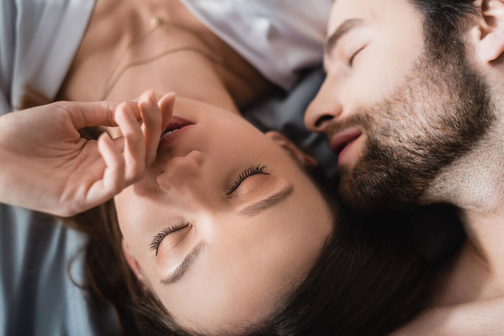 top view of young woman and bearded man with closed eyes lying on bed - Photo, Image