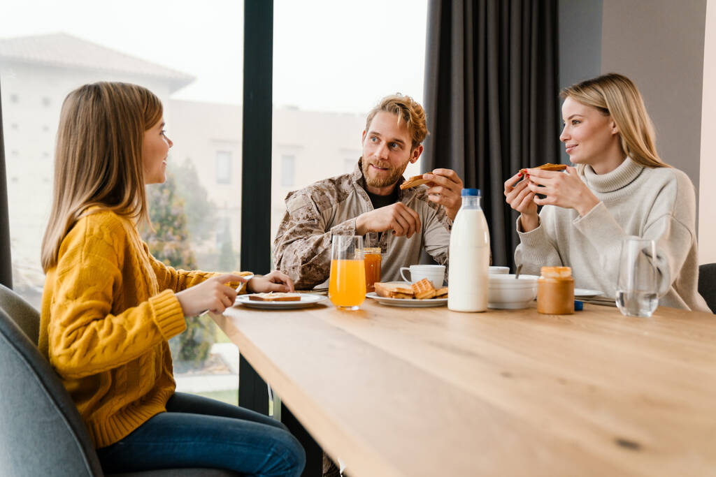 Kaunis onnellinen perhe puhuu ja hymyilee syödessään aamiaista kotona - Valokuva, kuva