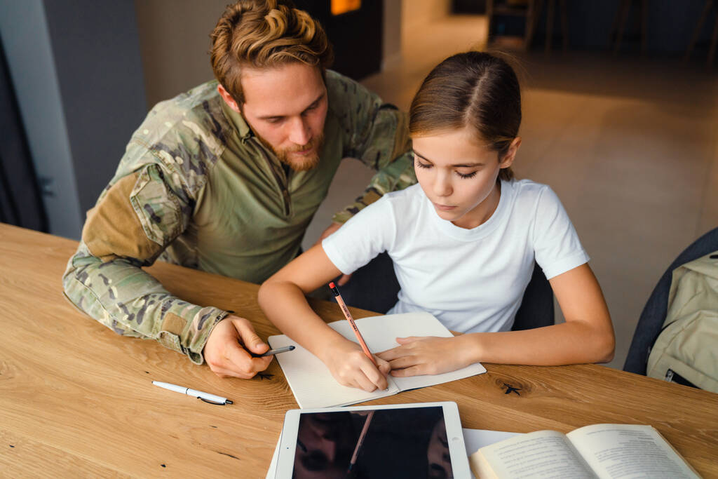 Masculine focused military man doing homework with her daughter at home - Photo, Image