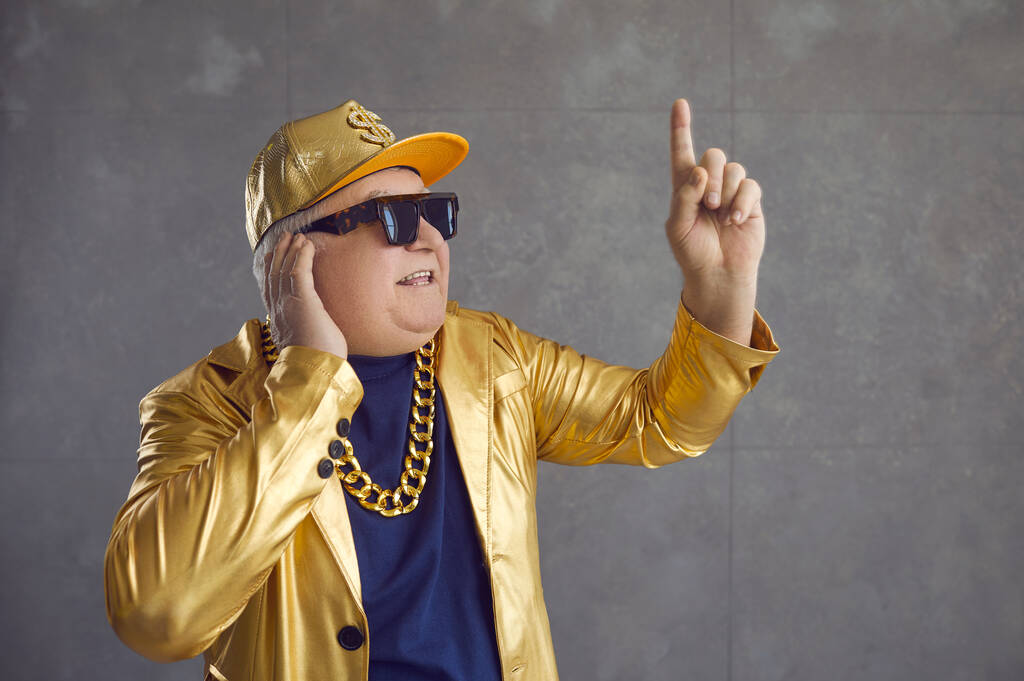 Смешной старший DJ в золотой куртке, бейсболке и цепочке ожерелье смешивая музыку на дискотеке - Фото, изображение