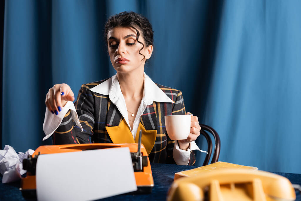 stylish journalist with coffee cup near vintage typewriter on blue background - Photo, Image