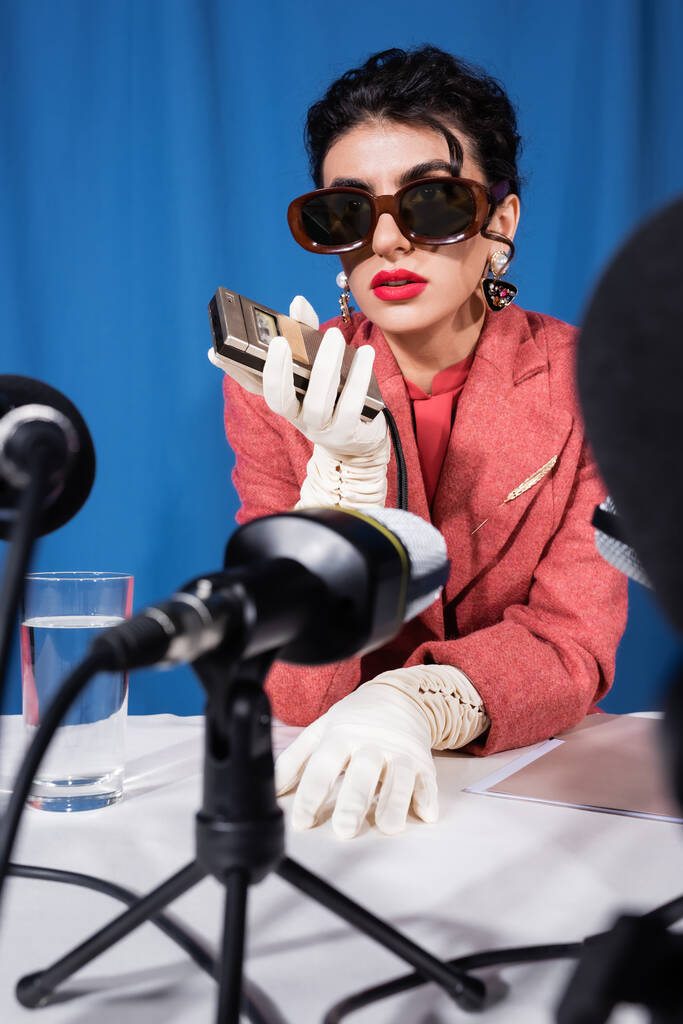 rozmazané mikrofony v blízkosti retro stylu žena držící hlasový záznam během rozhovoru na modrém pozadí - Fotografie, Obrázek