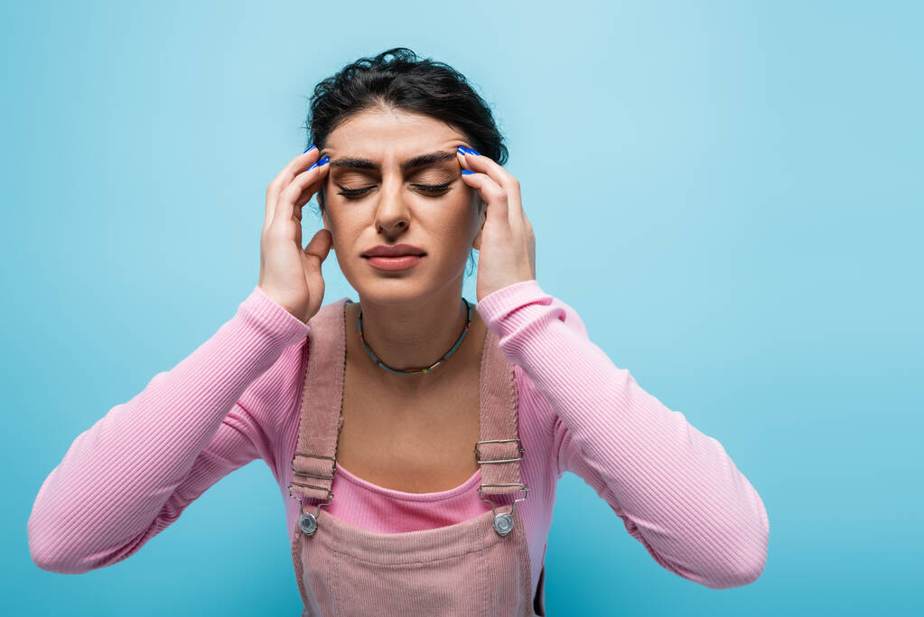 jeune femme avec les yeux fermés touchant la tête tout en souffrant de migraine isolé sur bleu - Photo, image