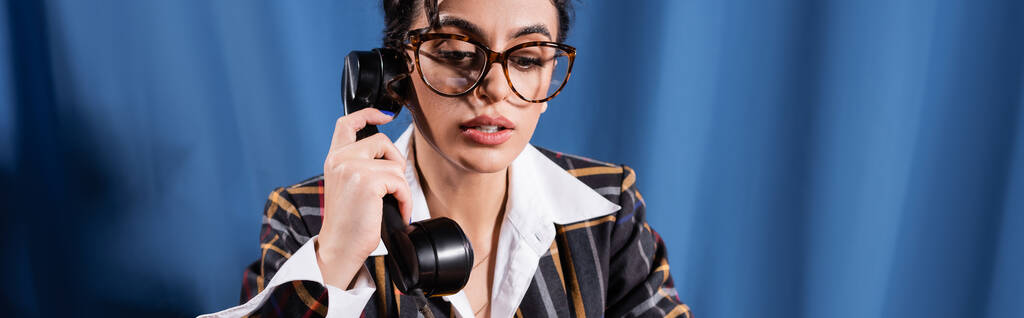 reportera con estilo en ropa vintage y gafas con auricular en el fondo azul, pancarta - Foto, Imagen