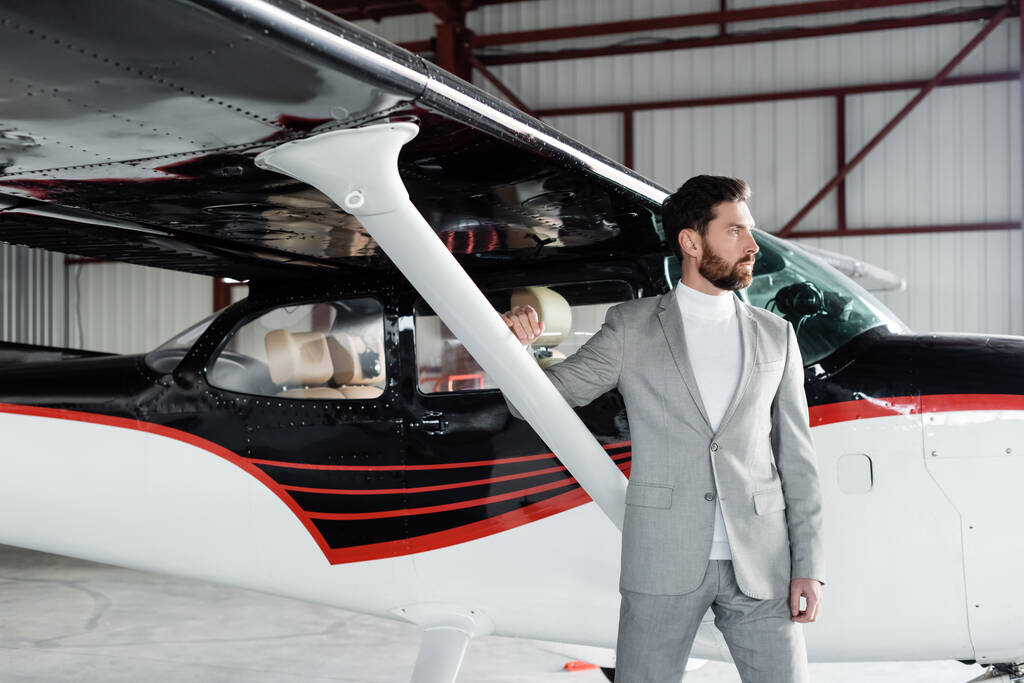 Selbstbewusster bärtiger Geschäftsmann im Anzug steht neben modernem Hubschrauber - Foto, Bild