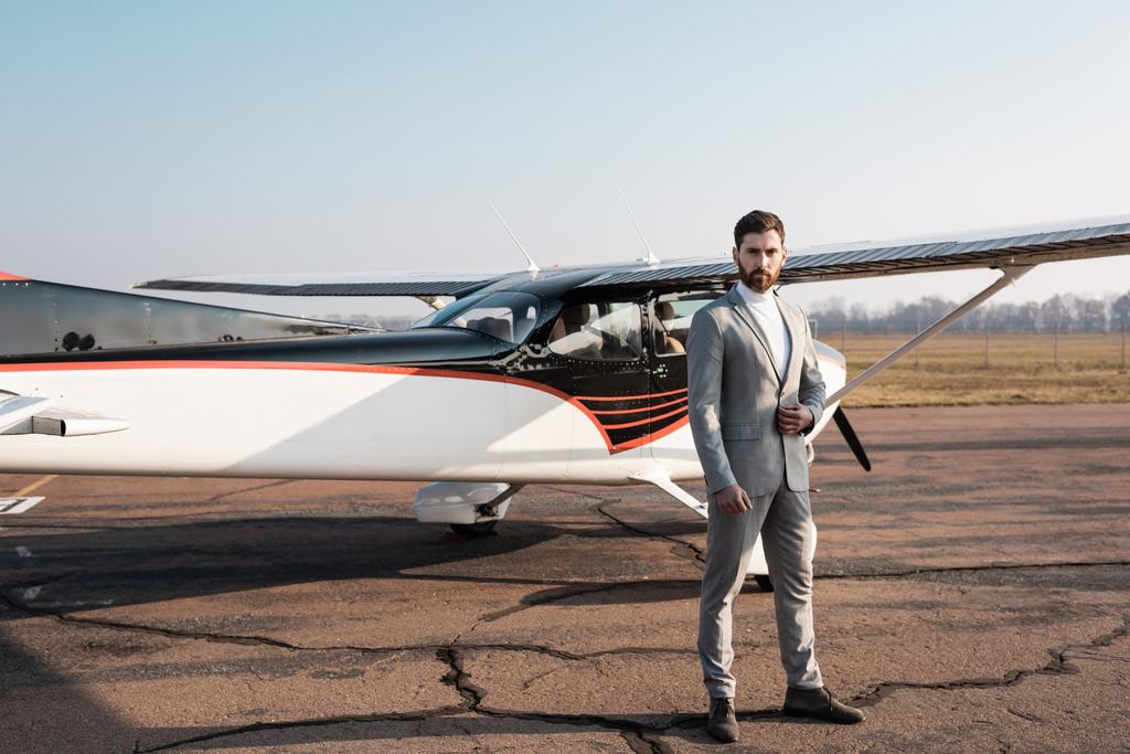 full length of confident businessman standing near modern helicopter and adjusting blazer - Photo, Image