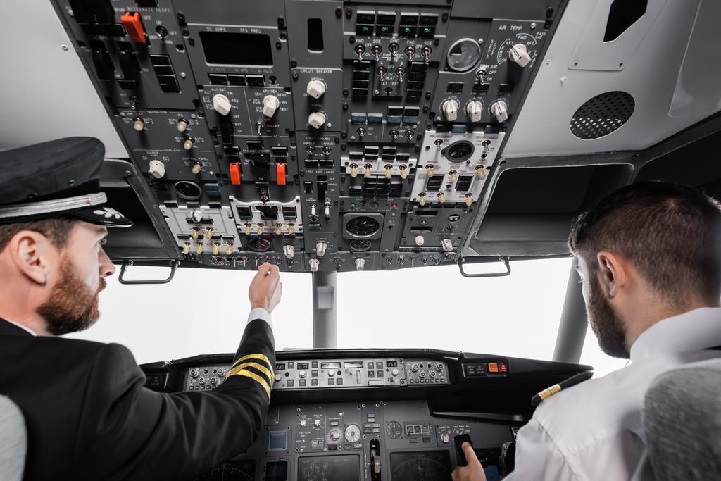γενειοφόρος πιλότος σε καπάκι που φθάνει εναέρια πάνελ κοντά συγκυβερνήτης σε προσομοιωτή αεροπλάνου  - Φωτογραφία, εικόνα