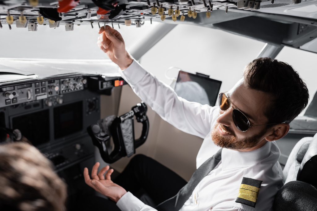 веселый пилот в солнцезащитных очках достигает верхней панели рядом со вторым пилотом в симуляторе самолета - Фото, изображение