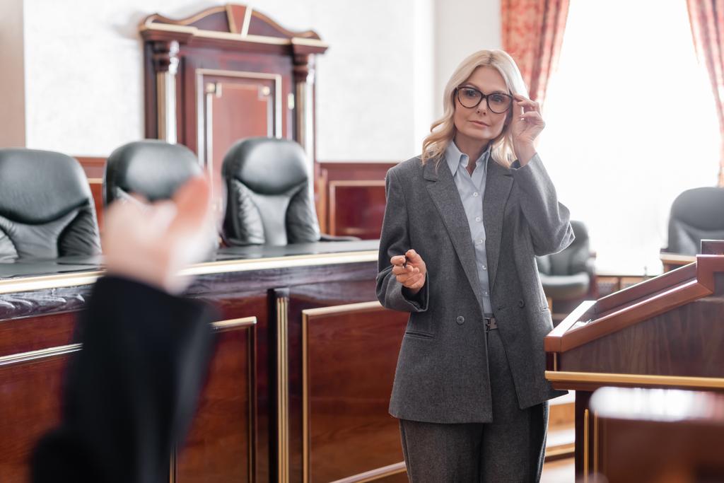 érett ügyvéd mutató kézzel és beállítása szemüveg kihallgatása során tanú bíróság előtt - Fotó, kép