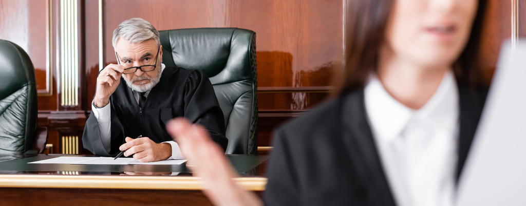 старший суддя коригує окуляри, дивлячись на прокурора на розмитому передньому плані, банер
 - Фото, зображення