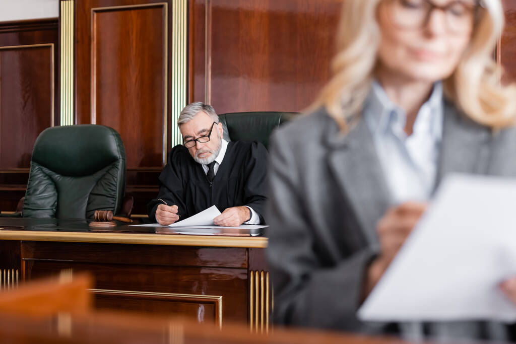 starší soudce čtení žaloby v blízkosti advokáta na rozmazané popředí - Fotografie, Obrázek
