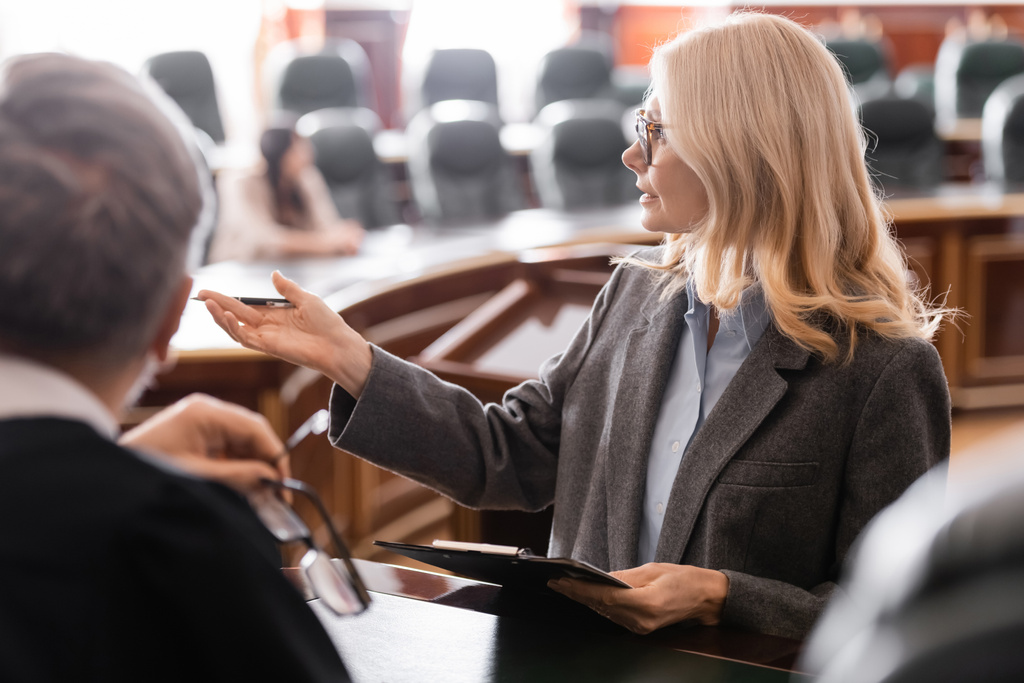Anwalt mittleren Alters zeigt mit der Hand in die Nähe des grauhaarigen Richters im Gerichtssaal - Foto, Bild