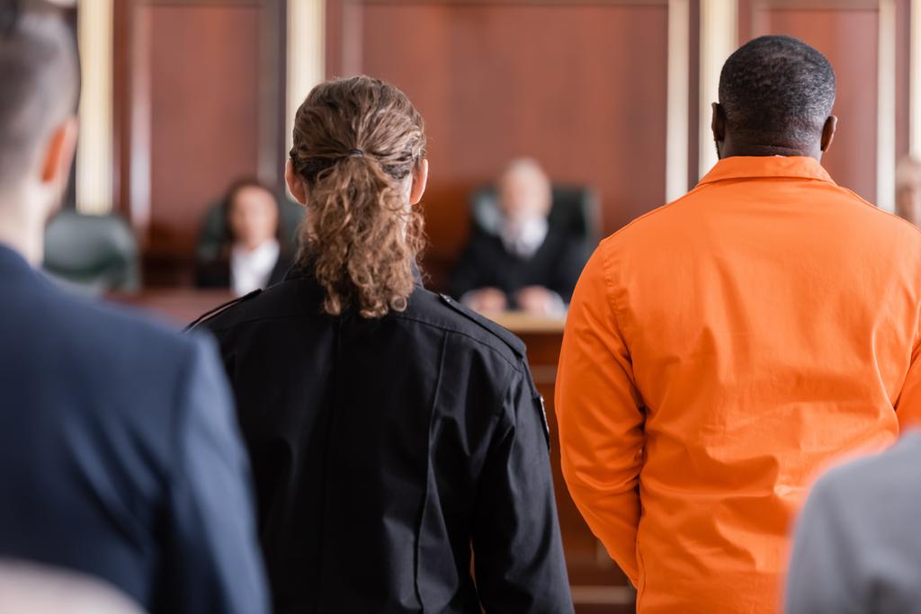 на задньому плані звинувачений афроамериканець біля вартових і розмитих присяжних у залі суду. - Фото, зображення