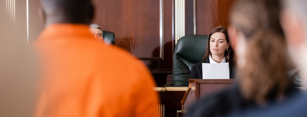 прокурор зачитывает документ рядом с судьей и обвиняет африканского американца на размытом переднем плане, баннер - Фото, изображение