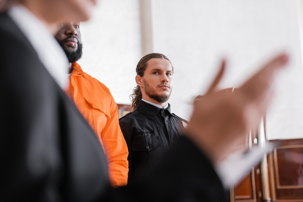 alguacil mirando borrosa fiscal mientras de pie cerca acusado africano amrican hombre en la corte - Foto, imagen