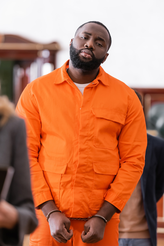 esposado afroamericano hombre en naranja cárcel uniforme en tribunal en borrosa primer plano - Foto, Imagen