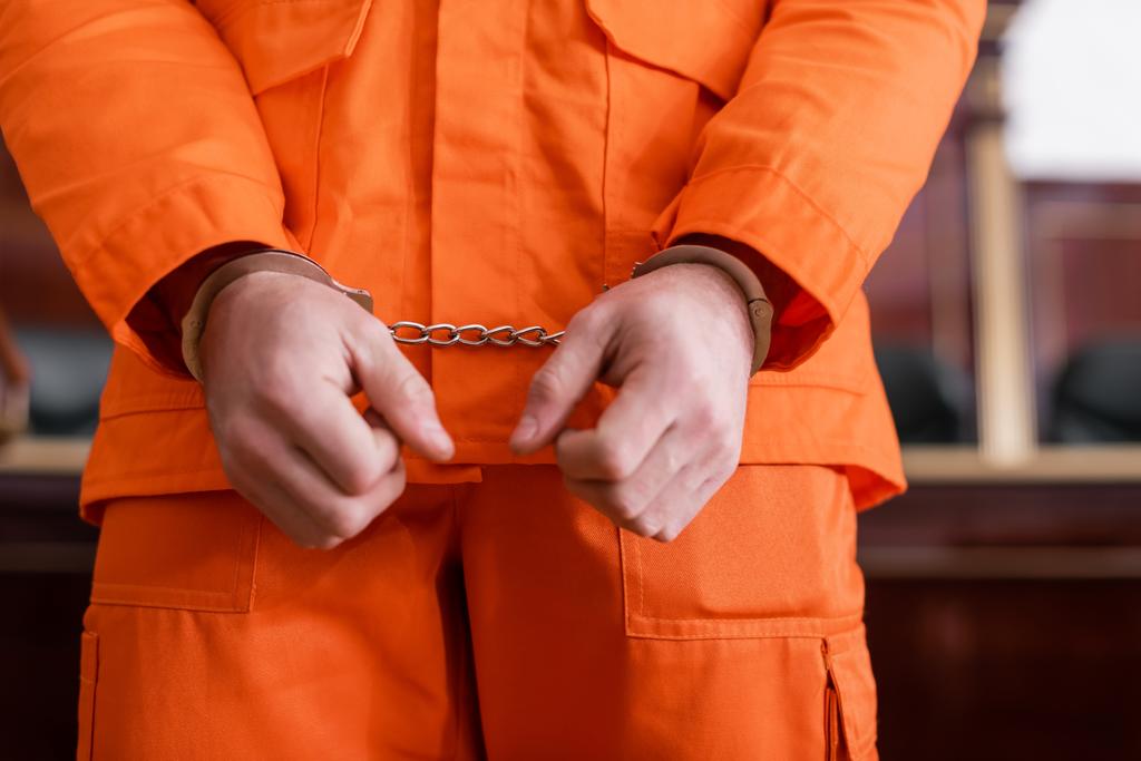 rajattu näkymä syytetystä miehestä käsiraudoissa ja oranssi vankilan univormu oikeudessa - Valokuva, kuva
