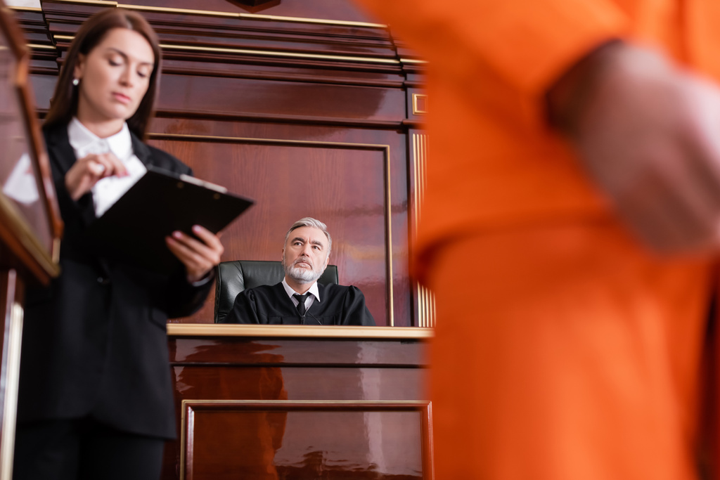 procurador olhando para prancheta perto de homem desfocado e juiz sênior em segundo plano - Foto, Imagem
