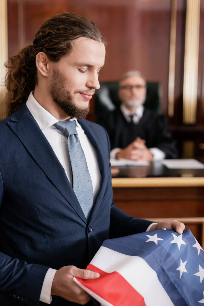 Positiver Anwalt hält US-Fahne im Gerichtssaal in der Nähe des obersten Richters vor unklarem Hintergrund - Foto, Bild