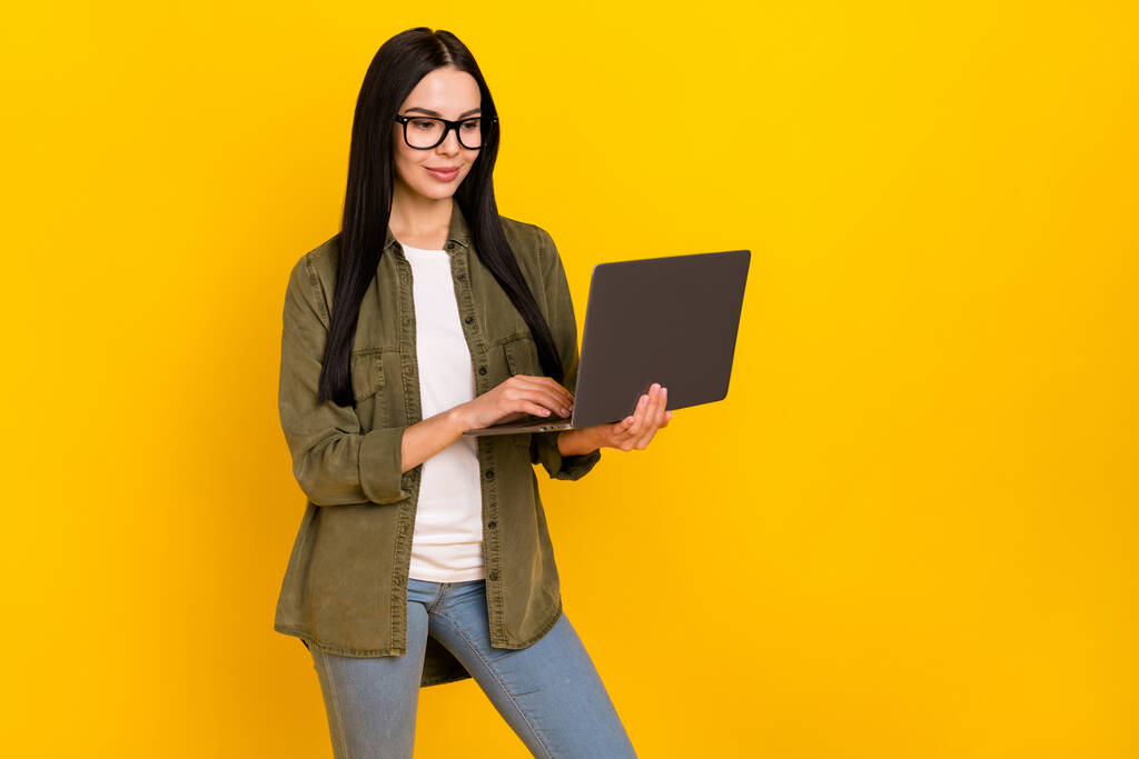Photo of nice millennial lady wygląd laptop nosić okulary khaki koszula dżinsy izolowane na żółtym tle - Zdjęcie, obraz