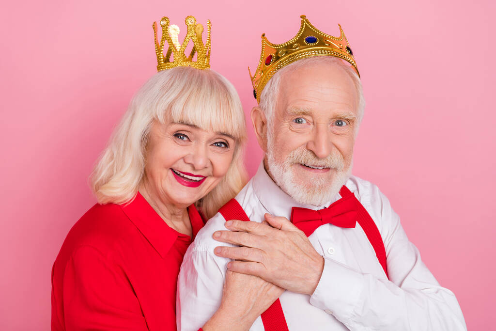 Portrait d'attrayant couple aux cheveux gris joyeux portant tiare étreinte isolé sur fond rose couleur pastel - Photo, image