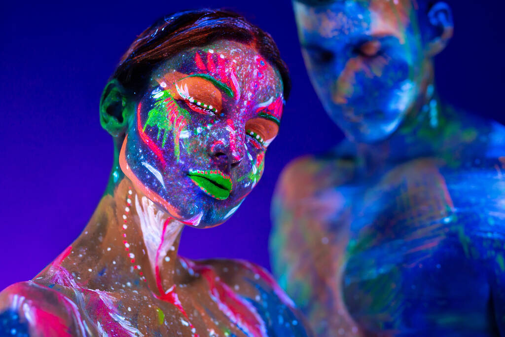 Portrait of a beefy man and woman painted in ultraviolet powder. Body art glowing in ultraviolet light. - Photo, Image