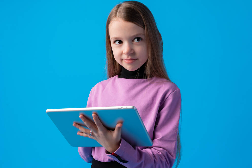 Menina usa um tablet digital em um fundo azul - Foto, Imagem