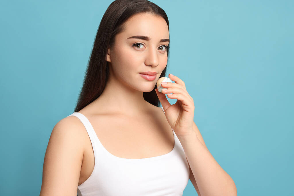 Young woman applying lip balm on turquoise background - Photo, Image
