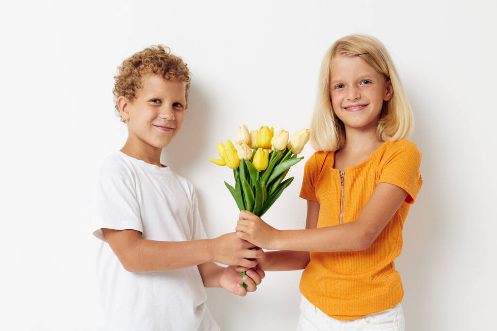 Leuke stijlvolle kinderen met een boeket bloemen cadeau verjaardag vakantie kindertijd licht achtergrond - Foto, afbeelding