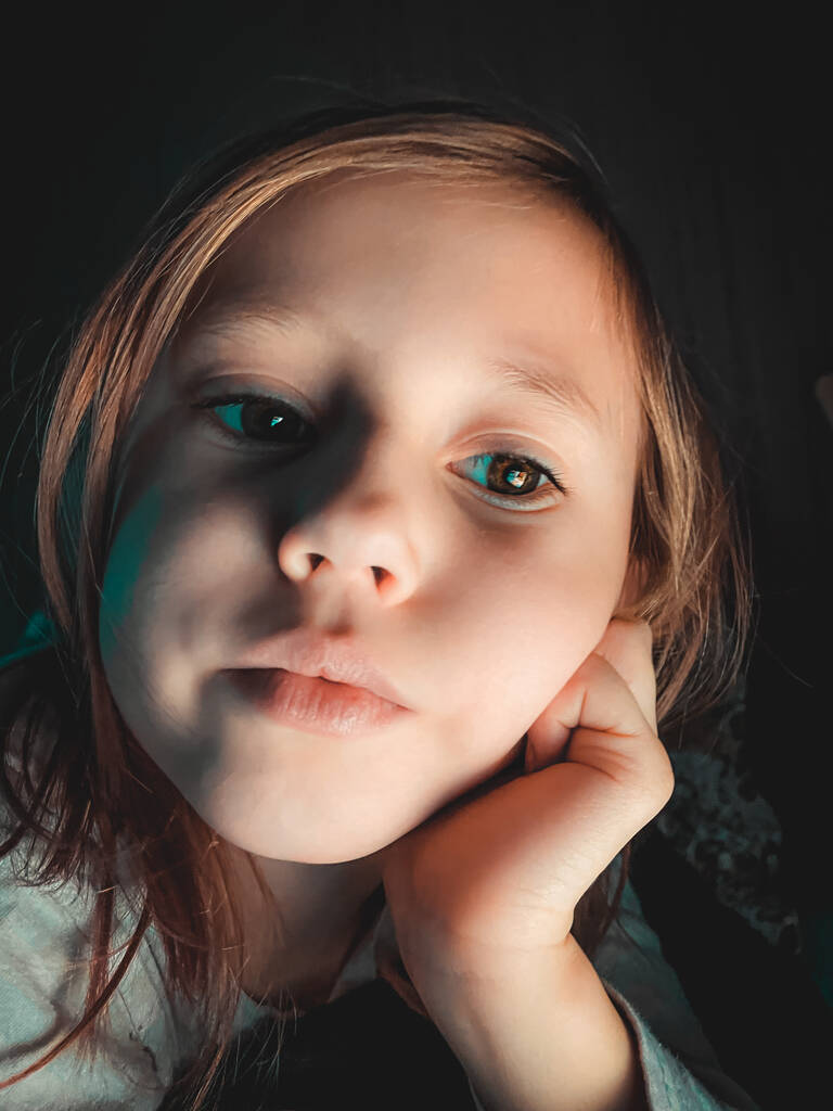 Kis kaukázusi lány mosolyog, és nézi a kamera este a sötétben az ágyban, életmód fotózás otthon, szelektív fókusz és lágy fókusz - Fotó, kép