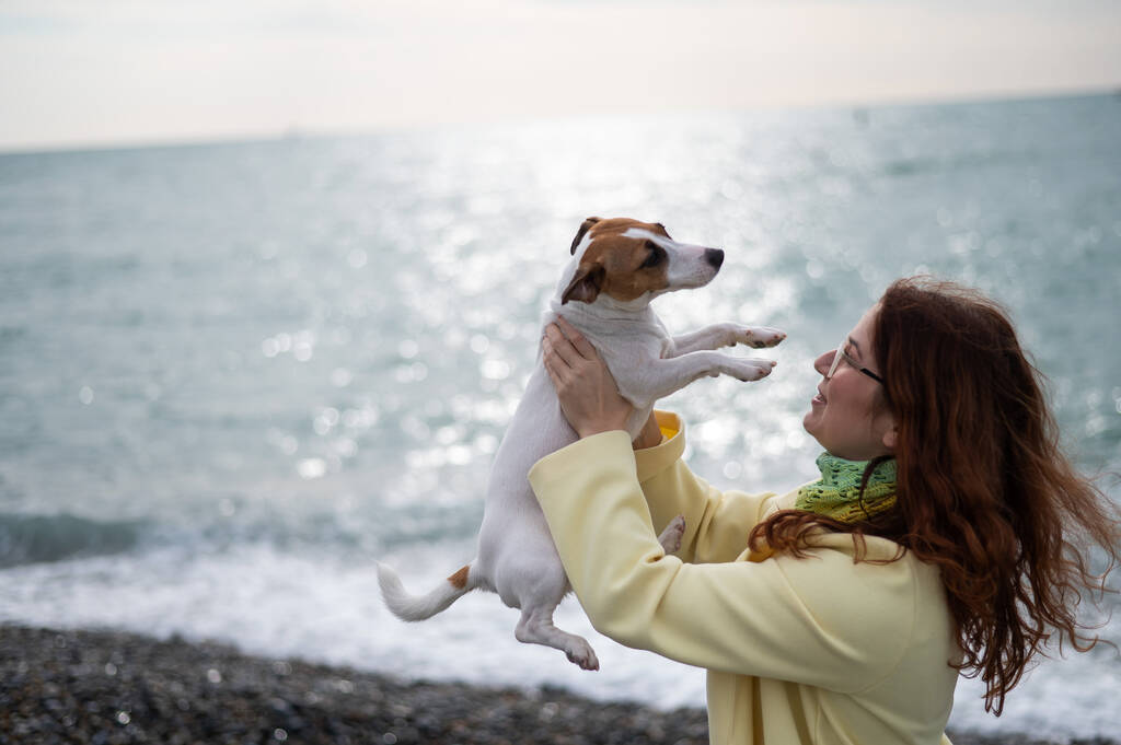 Kaukasische rothaarige Frau mit einem Jack Jack Russell Terrier am Meeresufer.  - Foto, Bild