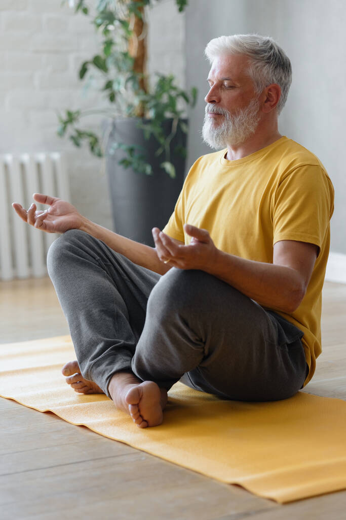 homem com cabelos grisalhos medita e faz exercícios respiratórios. aptidão desportiva e exercícios físicos para idosos - Foto, Imagem