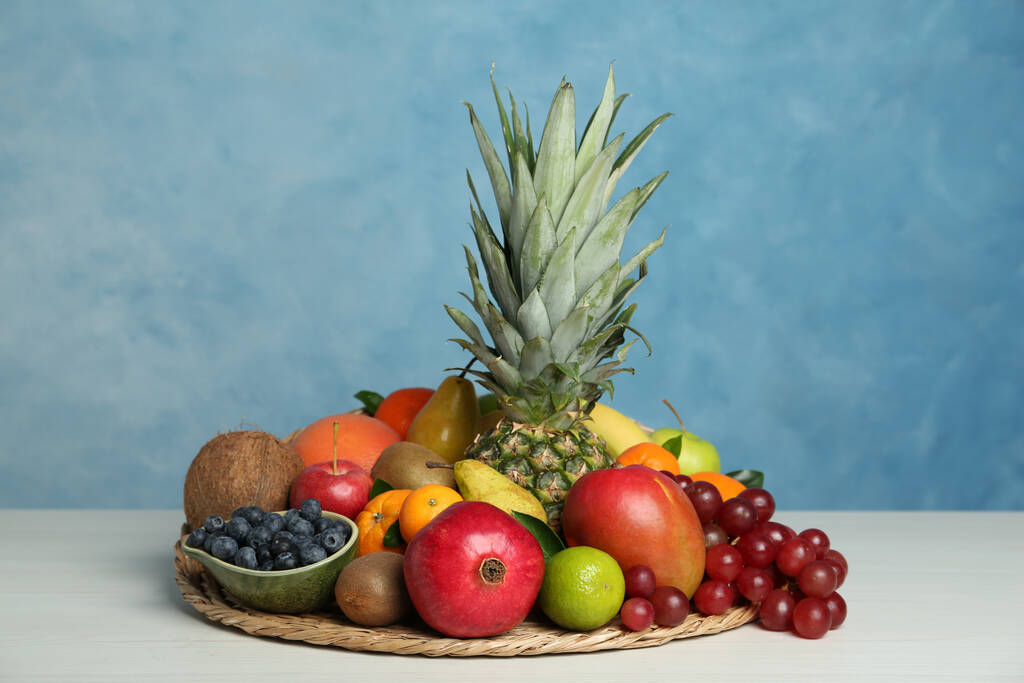 Auswahl an frischen exotischen Früchten auf weißem Holztisch vor hellblauem Hintergrund - Foto, Bild