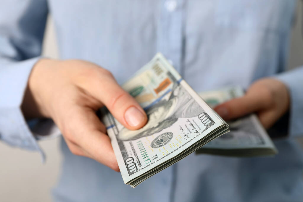 Kobieta licząca banknoty dolarowe na jasnym tle, zbliżenie - Zdjęcie, obraz