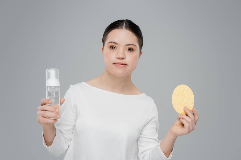 Mujer con síndrome de Down sosteniendo espuma limpiadora y esponja aislada en gris  - Foto, Imagen