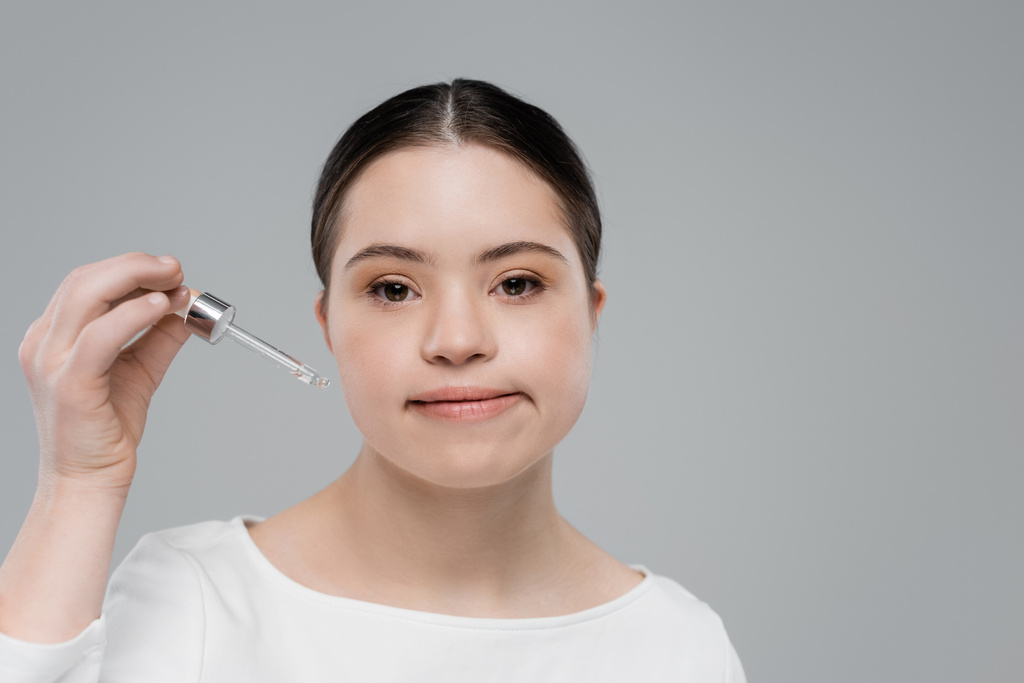 Woman with down syndrome holding dropper of cosmetic serum isolated on grey  - Photo, Image