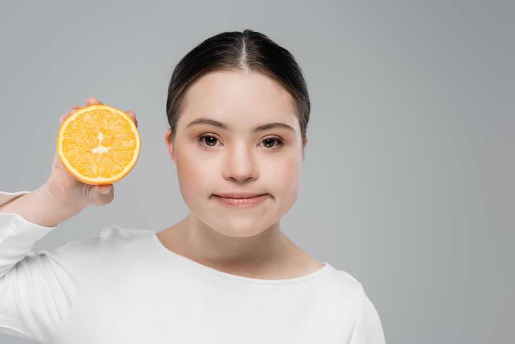 Mujer joven con síndrome de Down sosteniendo naranja aislada en gris  - Foto, Imagen