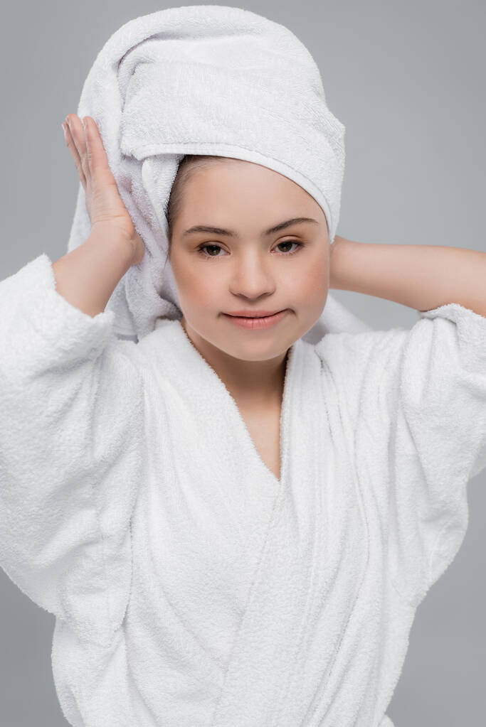 Mulher com síndrome de down em roupão de banho segurando toalha na cabeça isolada em cinza  - Foto, Imagem