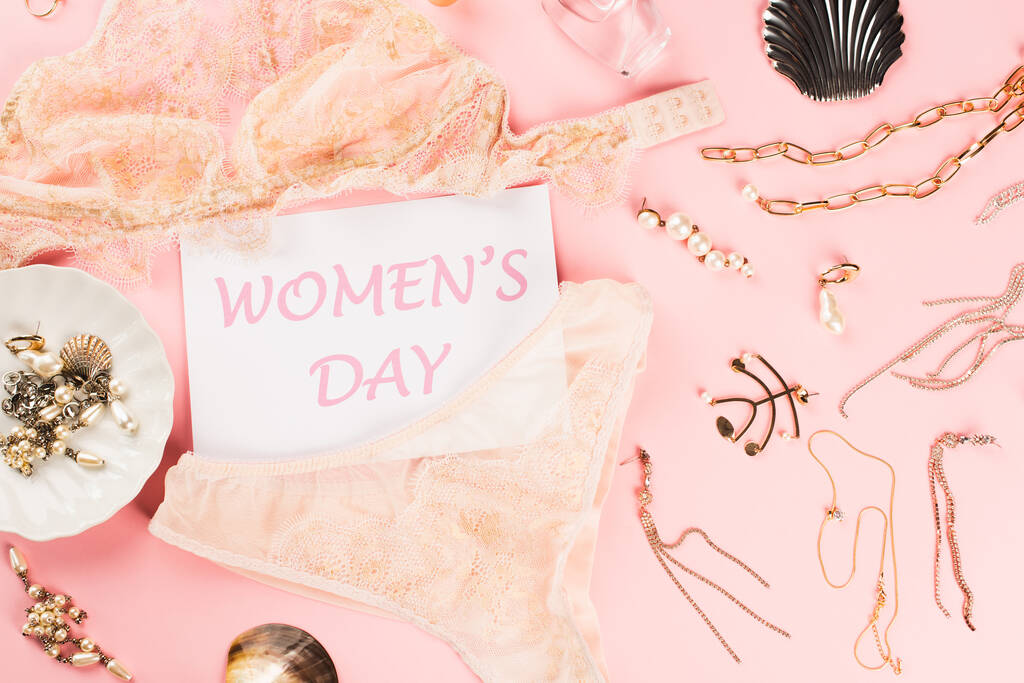 Вид сверху на открытку с женскими дневными нарядами рядом с золотыми аксессуарами и бельем на розовом фоне  - Фото, изображение